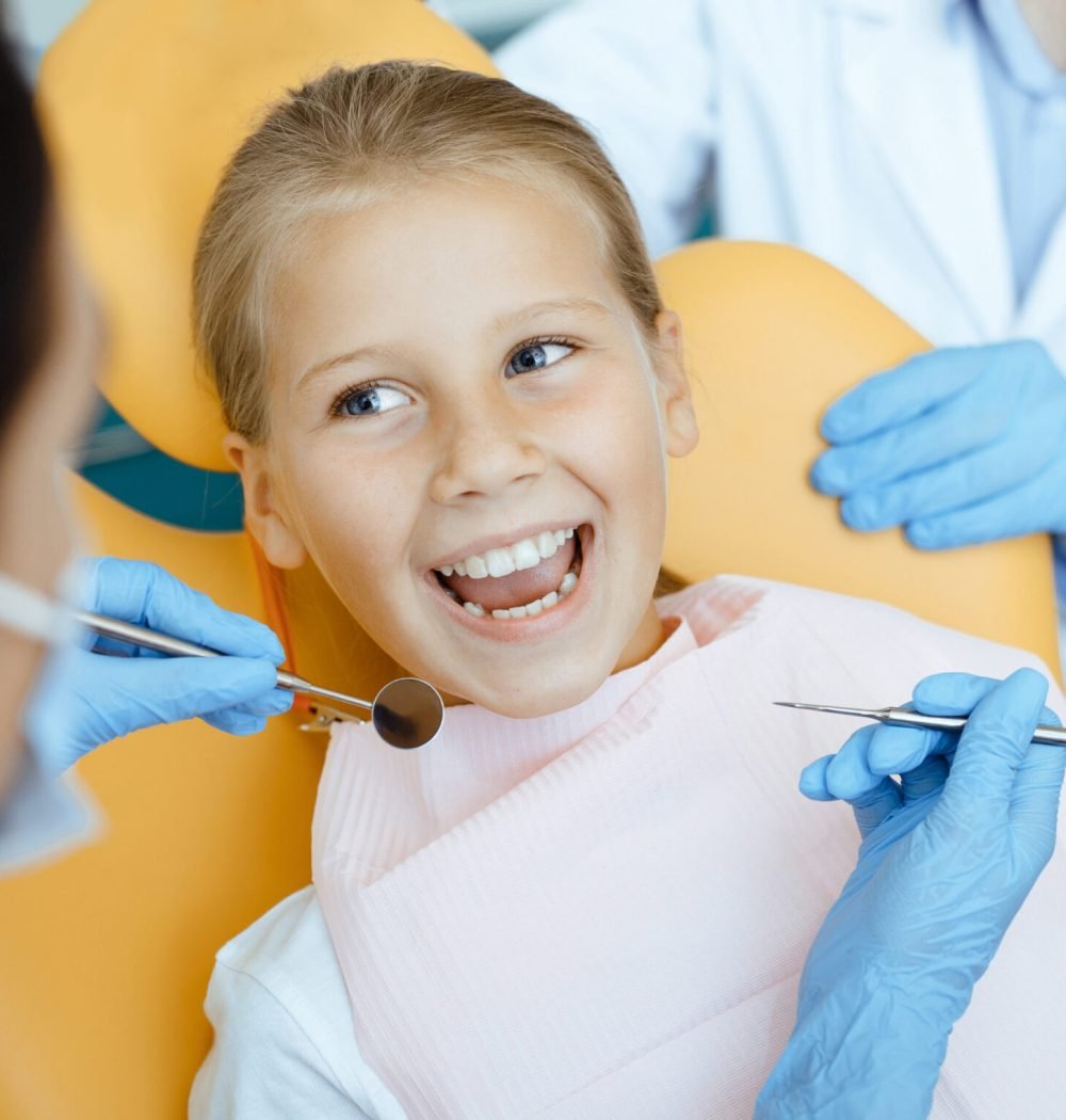 Perfect teeth after dental treatment. Cute little girl in chair opens her mouth and looks at doctor woman in protective mask with rubber gloves with medical instruments in her hands, close up, cropped